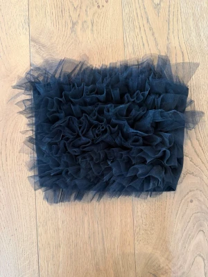 Svart bandeau topp med volang - Svart bandeau topp med volang framsida, från Gina tricot. Toppen är ärmlös och har en tight passform. Perfekt för dig som vill sticka ut med en cool och festlig look.