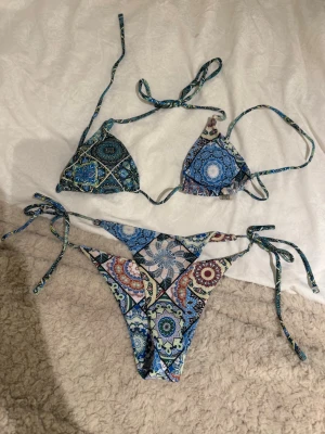 Färgglad bikini med mönster och knyt - Snygg bikini med färgstarkt, bohemiskt mönster i blått, grönt och inslag av rött. Klassisk trekantsmodell upptill och knyt i sidorna på underdelen. Perfekt för stranden eller poolen!