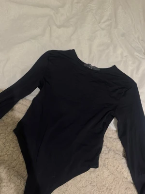 Svart långärmad body - En stilren svart body med långa ärmar och rund halsringning. Perfekt att styla med jeans eller kjol för en enkel och snygg look. Mjukt och stretchigt material som sitter bekvämt mot kroppen.