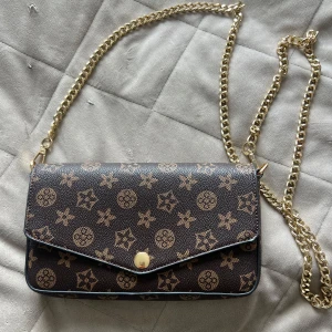 Vintage purse med wallet - Snygg brun axelväska med guldigt kedjeband och klassiskt mönster i beige. Väskan har kuvertformad front med tryckknapp och matchande plånbok. Insidan är röd med flera kortfack. Perfekt för dig som vill ha en stilren och trendig accessoar.