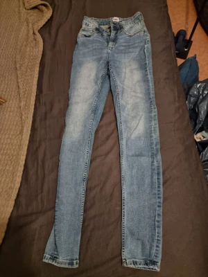 Blå skinny jeans XS - Säljer ett par blå skinny jeans från Lager 157 i storlek XS. Jeansen har klassisk femficksdesign, normalhög midja och snygga slitningar framtill. Tillverkade i stretchigt denimtyg för en bekväm passform. Perfekta till en avslappnad och trendig look. Modellen snake