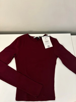 Vinröd långärmad topp  - En enkel och stilren vinröd långärmad topp från Gina Tricot. Modellen är tight med rund halsringning. Materialet är mjukt och stretchigt.