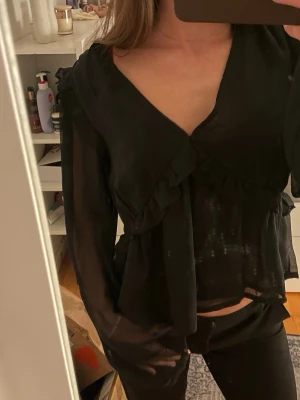 Svart blus med v-ringning - Superfin svart blus med v-ringning och volanger! Genomskinlig i ärmarna och i ryggen!! Endast använd ett fåtal gånger☺️