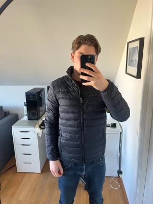 Mörkblå dunjacka från Berkeley - Säljer en mörkblå dunjacka från Berkeley. Jackan har dragkedja framtill och är tillverkad i ett lätt, glansigt material som håller värmen under kalla dagar. Perfekt för våren. Det finns även en två innerfickor som är rätt stora.