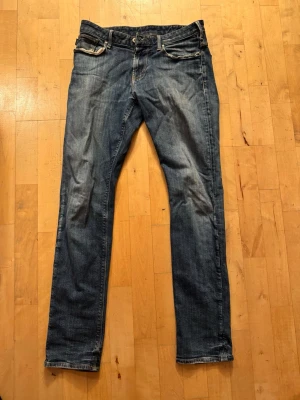 Armani jeans blå - Snygga blå jeans från Armani med raka ben och klassisk femficksdesign. Jeansen har slitningar och ljusare partier framtill för en cool, använd look. Tillverkade i denim med kontrastsömmar och logga på bakfickan. Storlek 29