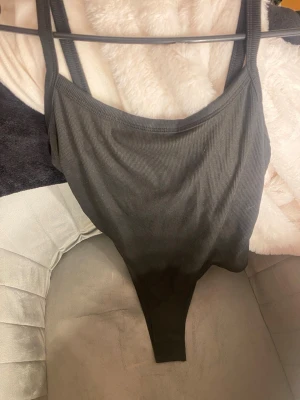 Svart ribbad body med tryckknappar - Snygg svart ribbad body med smala axelband och rundad urringning. Bodyn har praktiska tryckknappar i grenen för enkel på- och avklädning. Tillverkad i stretchigt material som sitter tight och bekvämt mot kroppen. Perfekt basplagg till garderoben.