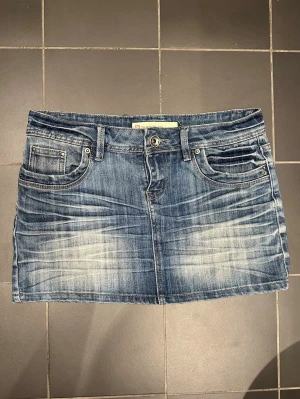 Blå jeanskjol med fickor - Snygg blå jeanskjol från FB sisters med bälteshällor, cool detalj vid etiketten och knappstängning framtill. Kjolen har låg midja, slitna detaljer och kontrastsömmar för en cool look. Perfekt till sneakers eller boots. Den är i väldigt bra skick men har några fläckar på baksidan som syns på bild 2-3. Midjemått tvärs över: ca 38cm