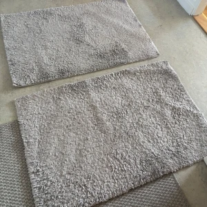 Två grå fluffiga mattor - Säljer två rektangulära mattor i mjukt, fluffigt material. Mattorna är ljusgrå och har en enkel, stilren design utan mönster. Perfekta att ha i sovrummet, hallen eller badrummet för extra komfort under fötterna. Ena lite trasig kan säljas styckvis 