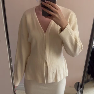 Beige v-ringad kofta i mjukt material med kjol - Stickad kofta med metall hooks, och kjol set. Slits på sidan. Oanvänd.