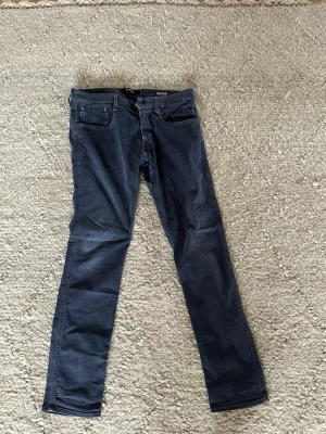Mörkblå raka jeans från Replay, modellen är Anbass. Storlek w33 l32 - Snygga mörkblå jeans från Replay med rak passform och klassisk femficksdesign. Jeansen har diskreta sömmar och en patch med logga bak i midjan. Tillverkade i ett mjukt bomullsmaterial med lite stretch för extra komfort.