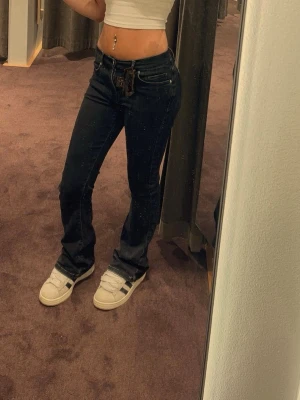 Svarta lågmidjade bootcut jeans  - Snygga svarta jeans med en bootcut passform och låg midja. Klassisk femficksmodell och bälteshällor. Perfekta för en avslappnad och trendig look. Inga synliga loggor eller märken. Materialet ser ut att vara denim.