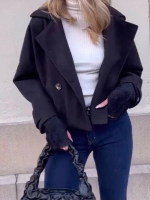 Svart kort kappa med bred krage - Stilren svart kappa i kort modell med bred krage och dubbelknäppning framtill. Kappan har två knappar och raka ärmar, perfekt för en trendig och enkel look. Passar till både jeans och kjol. Materialet ser ut att vara ullblandning. Står ingen storlek passa mig som bruka ha xs-s