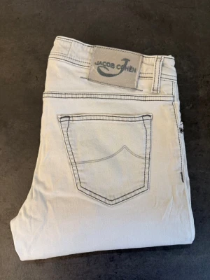 Vita jeans från Jacob Cohen W35 - Snygga vita jeans från Jacob Cohen med klassisk femficksmodell och kontrasterande sömmar. Jeansen har rak passform och är tillverkade i ett mjukt bomullstyg. Perfekta för en stilren och fräsch look. Skriv för mått!