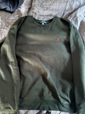 Svart sweatshirt från Polo Ralph Lauren - Tja! Svart sweatshirt från Polo Ralph Lauren med klassisk rund halsringning och lång ärm. Tröjan har en liten röd broderad logga på bröstet och är tillverkad i mjuk bomull. Perfekt för en avslappnad och stilren look.