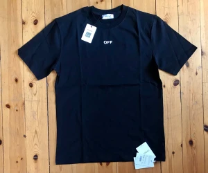 Svart Off-White t-shirt med tryck - Svart t-shirt från Off-White med liten vit 'OFF'-logga på bröstet och stort konstnärligt tryck på ryggen. Klassisk rund hals och korta ärmar. Tillverkad i mjuk bomull för en skön känsla. Perfekt för dig som gillar streetwear och unika detaljer.