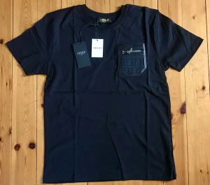 Svart Fendi t-shirt med ficka - Svart t-shirt från Fendi med kort ärm och en snygg bröstficka med Fendi-logga och dragkedjedetalj. Klassisk rund halsringning och stilren design, perfekt för en trendig look.