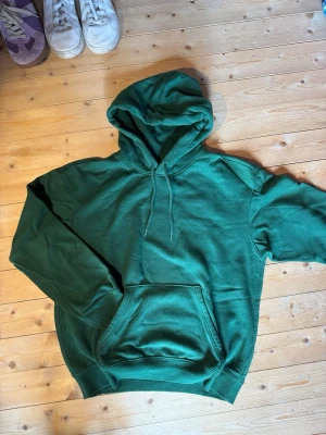 Grön hoodie  - Snygg grön hoodie med klassisk huva och dragsnören. Hoodien har en stor magficka framtill och ribbade muddar vid ärmslut och nederkant. 