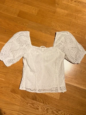 Vit broderad blus med puffärm H&M - Superfin vit blus från H&M med broderade detaljer och puffiga korta ärmar. Toppen har v-ringning och är tillverkad i bomull med spetsmönster. Perfekt för en trendig och romantisk look.