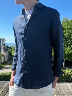 Mörkblå Massimo dutti linneskjorta med knappar - (MODDELEN:185 och väger 75kg)Snygg mörkblå skjorta i linne med klassisk krage och vita knappar. Skjortan har lång ärm och en avslappnad passform, perfekt för varma dagar. Enkel och stilren design som funkar till det mesta.