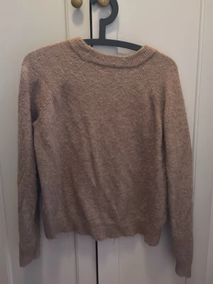 Beige stickad tröja från Zara - Mjuk och mysig beige stickad tröja från Zara med rund halsringning och långa ärmar. Tröjan har en lätt fluffig struktur och ribbstickade detaljer vid hals, ärmslut och nederkant. Perfekt för lager-på-lager under kyliga dagar.