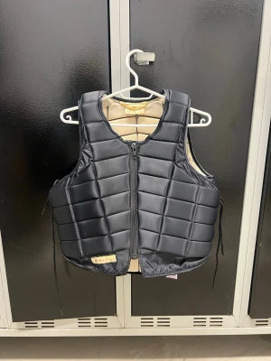 Svart quiltad ridväst från Racesafe - Säljer en svart quiltad ridväst från Racesafe med en dragkedja framtill och justerbara snören i sidorna. Västen är i väldigt bra skick! Storleken är Adult small.