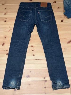 Levi's jeans 501 - Säljer ett par mörkblå jeans från Levi's i modellen 501. De är i bra skick utöver slitningar i hälarna. Storlek: W28 L32. Hör gärna av dig vid frågor!