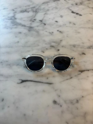 S&T 001 Blanc solglasögon  - Stig fram med stil och självförtroende i våra solglasögon 001. Med en elegant och modern design är dessa solglasögon det perfekta accessoaret för att komplettera din sommarlook. Tillverkade med högkvalitativa material och med omsorgsfullt utformade detaljer, erbjuder de inte bara en trendig estetik utan också överlägsen skydd mot solens strålar. Med sina mångsidiga och universellt smickrande form passar de alla ansiktsformer och ger en sofistikerad touch till varje outfit