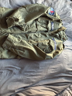 Polo militär jacka - Säljer en olivgrön vindjacka med tydliga militärvibbar från USAF. Jackan har flera praktiska fickor framtill, patchar på bröstet och ärmen samt klassisk krage. Perfekt för dig som gillar utility-stil och streetwear. Helt oanvänd nästan