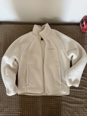 Vit jacka från Bershka - Mysig vit teddyjacka från Bershka med dragkedja framtill och två fickor. Jackan har hög krage och är tillverkad i fluffigt teddy-material som ger en cool och avslappnad look. Perfekt för att hålla värmen under kyliga dagar.
