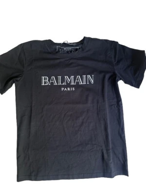 Balmain T-shirt - Tjo! Säljer denna feta svarta Balmain t-shirten med tryck i storlek M, sitter som S. Skick 10/10 oanvänd med tags och påse 🔥. Perfekt till dig som vill ha en lite lyxigare tröja till sommaren. Skriv vid frågor eller funderingar! /TA