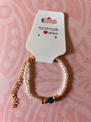 Pärlarmband med gulddetaljer - Snyggt handgjort armband med vita pärlor, guldfärgade detaljer och en grön pärla i mitten. Justerbar kedja i guldton för perfekt passform. Perfekt accessoar för att lyfta din stil.