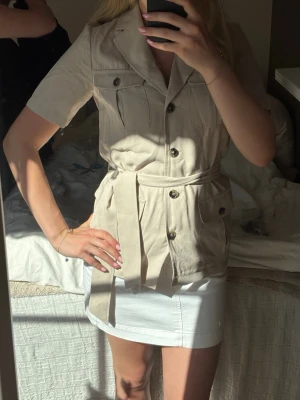 Beige utilityblus med knytskärp - Stilren beige utilityblus från Zara med korta ärmar, knappar framtill och fyra fickor. 