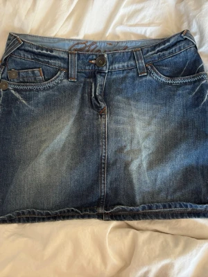 Blå jeanskjol med fickor - Snygg blå jeanskjol med klassisk femficksdesign och dekorativa sömmar på bakfickorna. 