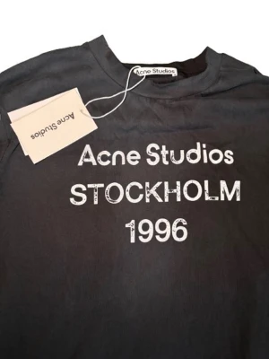 Svart långärmad topp Acne Studios - Svart långärmad topp från Acne Studios med vit text 'Acne Studios STOCKHOLM 1996' framtill. 