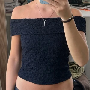 Mörkblå off shoulder topp - Trendig mörkblå off shoulder topp med smockat tyg och åtsittande passform. Toppen är axelbandslös och har en bred volangkant upptill. Perfekt för en stilren och modern look. Passar mig som xs/s.