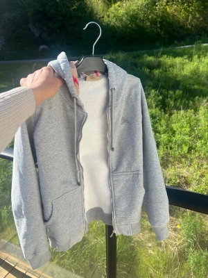 Grå zip-hoodie med fickor - En stilren grå hoodie med dragkedja och två stora fickor framtill. Tröjan har huva med dragsko och ribbade muddar vid ärmslut och nederkant. Perfekt för en avslappnad och sportig look. Priset kan diskuteras 😄
