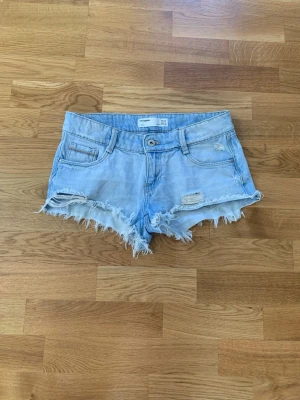 Ljusblå jeansshorts med slitningar - Säljer ett par ljusblå jeansshorts från Zara med fransiga kanter och slitna detaljer framtill. Storleken är XS/34 och har lite detalj på fickorna.