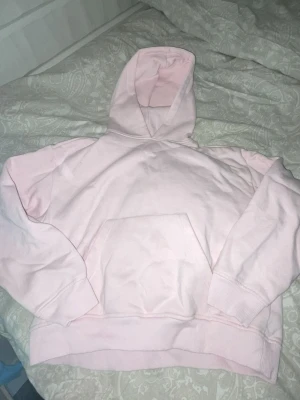 Ljusrosa hoodie med huva - Säljer en ljusrosa hoodie med klassisk känguruficka och huva. Hoodien har ribbade muddar vid ärmslut och nederkant. Perfekt för en avslappnad och trendig stil. Materialet känns mjukt och skönt mot huden.