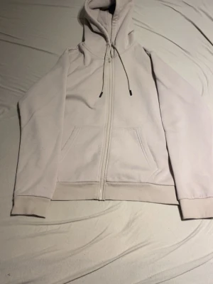 Ljusbeige zip hoodie med huva - En stilren ljusbeige hoodie med dragkedja framtill, huva med dragsko och två fickor. Perfekt för en avslappnad look. Mjuk bomullsblandning och ribbade muddar vid ärmslut och midja.