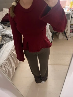 Vinröd topp med utsvängda ärmar - Snygg vinröd topp med långärmade utsvängda ärmar och markerad midja. Toppen har en peplum-liknande volang nertill och är tillverkad i ett mjukt, sammetsliknande material. Perfekt för dig som vill sticka ut med en trendig och bekväm look.