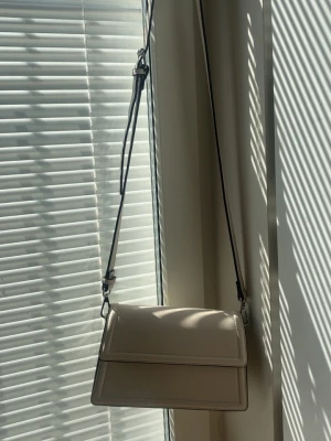 Beige/krämvit väska  - Stilren beige axelväska med justerbar rem.