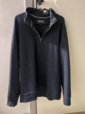 Mörkblå halvzip  - Mörkblå långärmad tröja från Pierre Balmain med halvzip och hög krage. Tröjan har en stilren design med ribbade muddar vid ärmslut och nederkant. Perfekt för en avslappnad men snygg look.