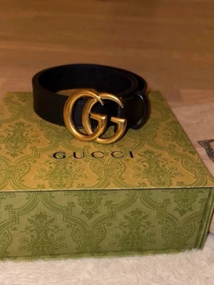 Svart Gucci bälte med GG-spänne - Snyggt svart bälte från Gucci med ikoniskt dubbelt GG-spänne i guld. Bältet är tillverkat i skinn och har en klassisk, stilren design som passar till många olika outfits. Perfekt accessoar för att lyfta din look. (Storlek 70)