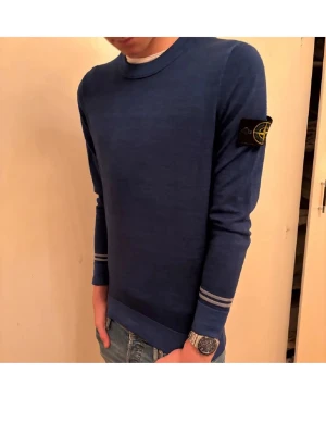 Blå tröja från Stone Island - Snygg blå tröja från Stone Island med rund hals och ikonisk logotyp på vänster ärm. Tröjan har smala grå ränder vid ärmslut och nederkant, och är tillverkad i mjukt material som känns skönt mot huden. Perfekt för en stilren och avslappnad look.