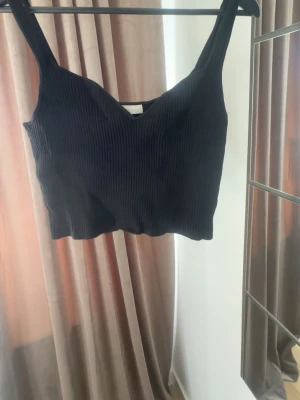Svart ribbad croppad linnetopp - Snygg svart croppad linnetopp med breda axelband från hm. Perfekt till vår/sommar, pris kan diskuteras.