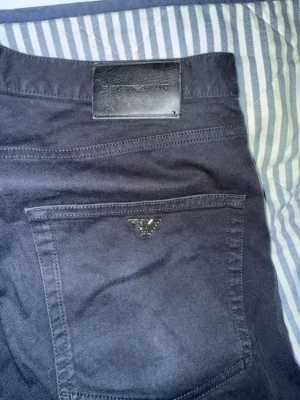 Mörkblå jeans från Emporio Armani - Snygga mörkblå jeans från Emporio Armani med klassisk femficksdesign och metallogo på myntfickan. Jeansen har raka ben och är tillverkade i ett mjukt denimtyg. Perfekta för dig som gillar stilrena och tidlösa plagg.