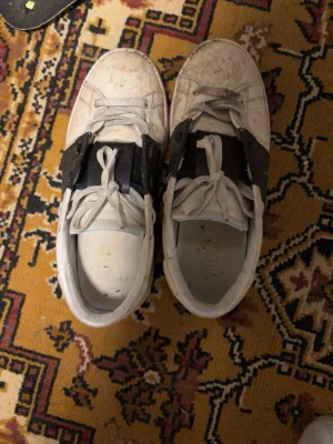 Vita sneakers med svarta detaljer - Snygga vita sneakers med svarta detaljer över snörningen. Klassisk låg modell med rund tå och vita skosnören. Perfekta för en streetwear-look och passar till det mesta i garderoben.