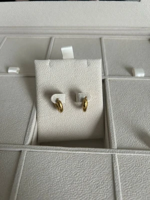 Guldpläterade små hoops örhängen Muli Collection  - Snygga små hoops örhängen i guldpläterad metall. De har en enkel och stilren design med rund form och blank finish. Perfekta för dig som gillar minimalistiska smycken och vill ha något som funkar till många olika looks.