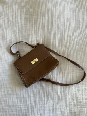 Brun axelremsväska  - Snygg brun handväska med avtagbar axelrem och guldfärgade detaljer. Fotad fläck inuti 