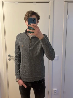 Mörkgrå stickad tröja med halvzip - Mörkgrå stickad tröja med halvzip och hög krage. Diskret logga på bröstet och ribbade muddar vid ärmslut och nederkant. Perfekt för lager-på-lager och enkel att matcha med jeans. Materialet är mjukt och bekvämt. Bara använd ett fåtal gånger.